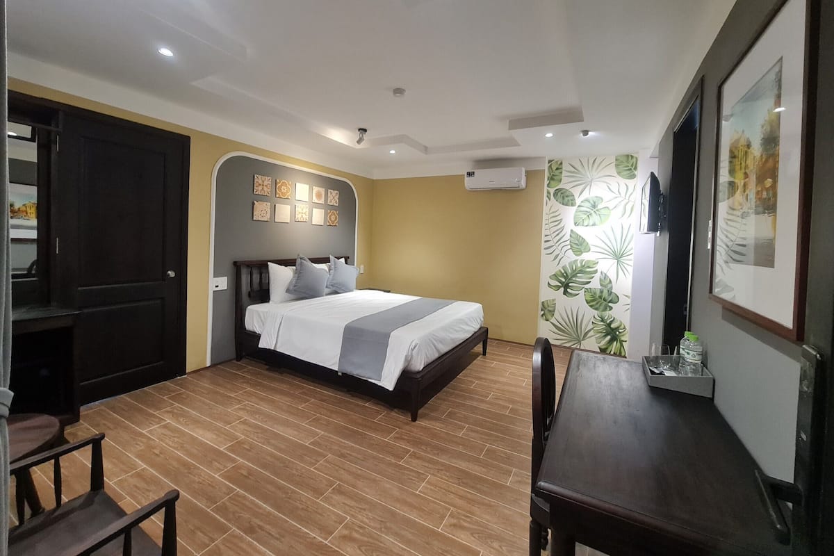 A hotel room with a bed, a desk, and a chair. There is a door and a wall with a plant pattern.