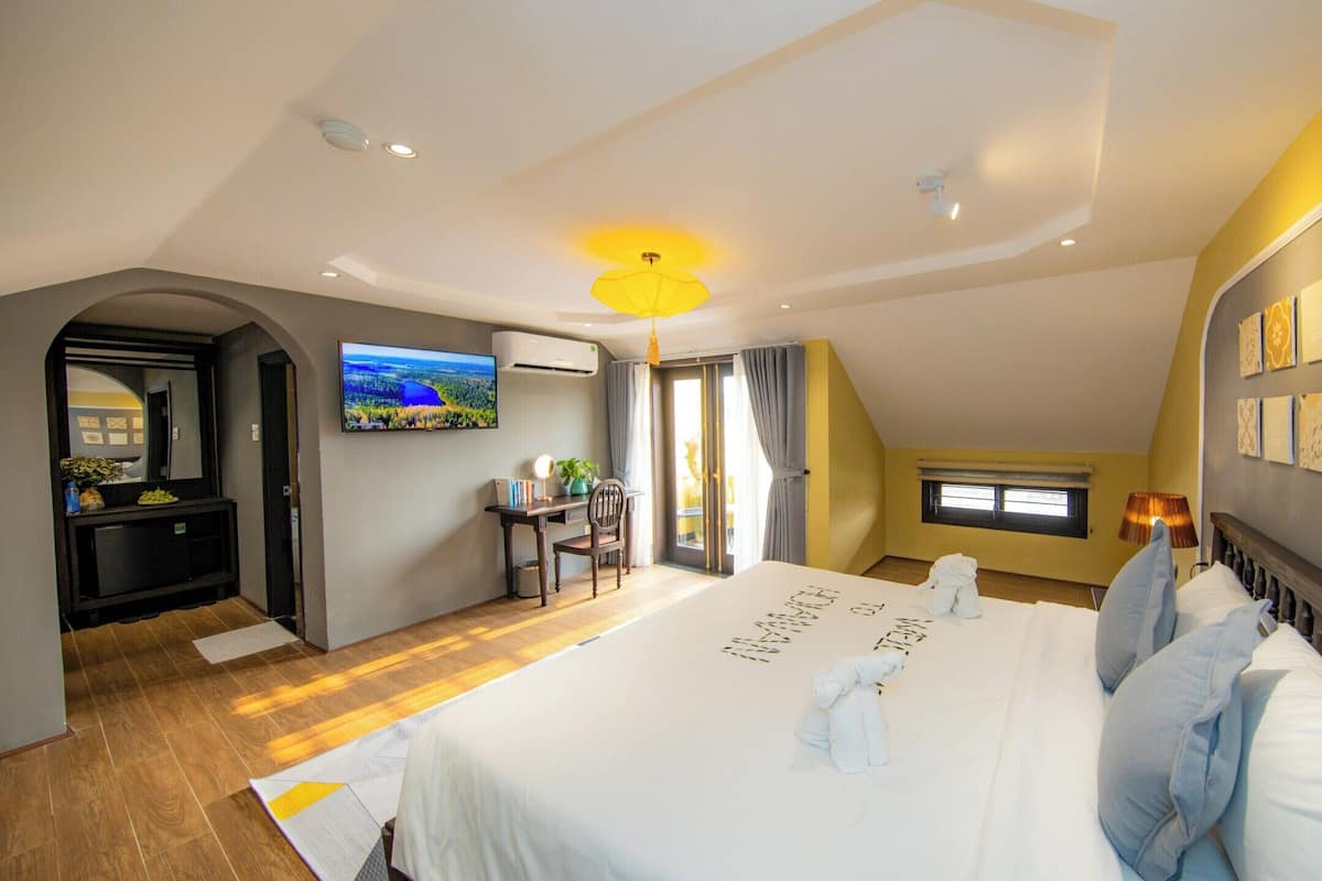 A bedroom with a large bed, a desk with a chair, a TV, and artwork on the walls.