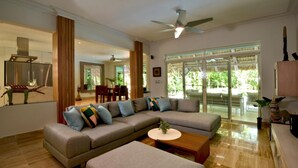 A modern living room with a sectional sofa, a coffee table, and a dining area visible through glass doors. - Tortuga Bay Villa - Close to the Beach and Golf (Punta Cana)