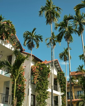 A multi-story building with balconies, surrounded by tall palm trees. - Anmira Hoi An – Village of Arts and Culture (Da Nang)