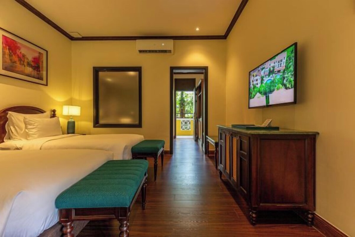 A hotel room with a bed, a desk, a chair, a bench, and a television on the wall.