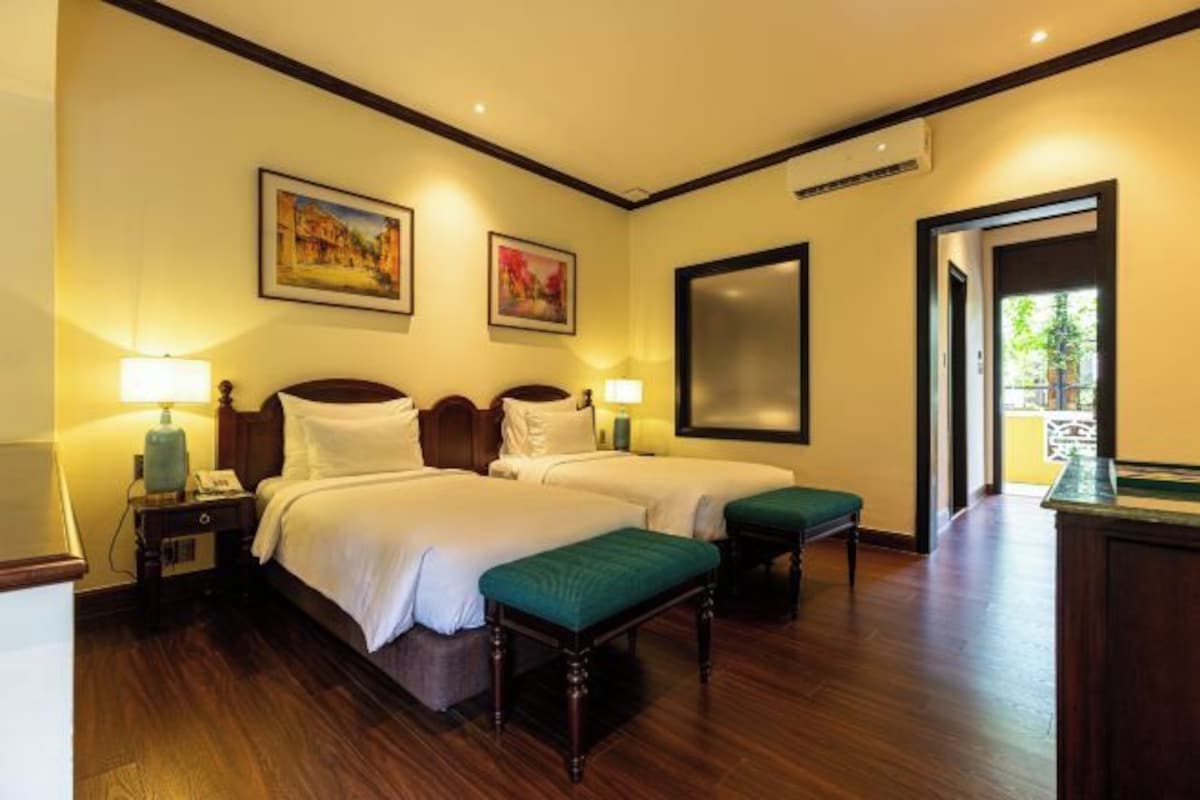 Habitación de hotel con dos camas, lámparas de noche, un banco y obras de arte en las paredes.