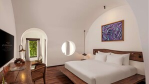Quarto de hotel moderno com cama de madeira, escrivaninha com TV de tela plana, espelho redondo e uma grande pintura abstrata na parede.