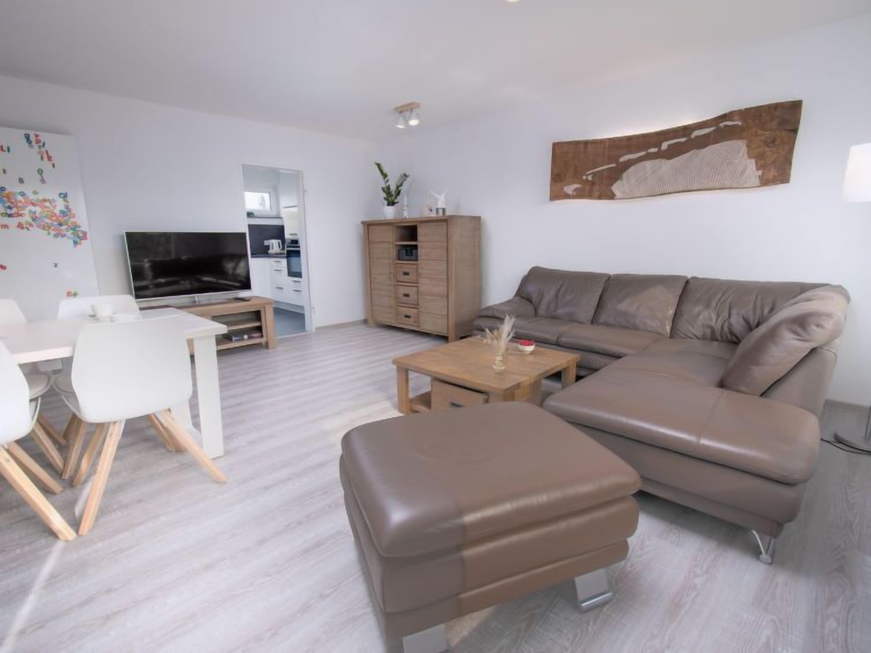 Ein modernes Wohnzimmer mit einer Couch, einem Hocker, einem Couchtisch und einem Fernseher.