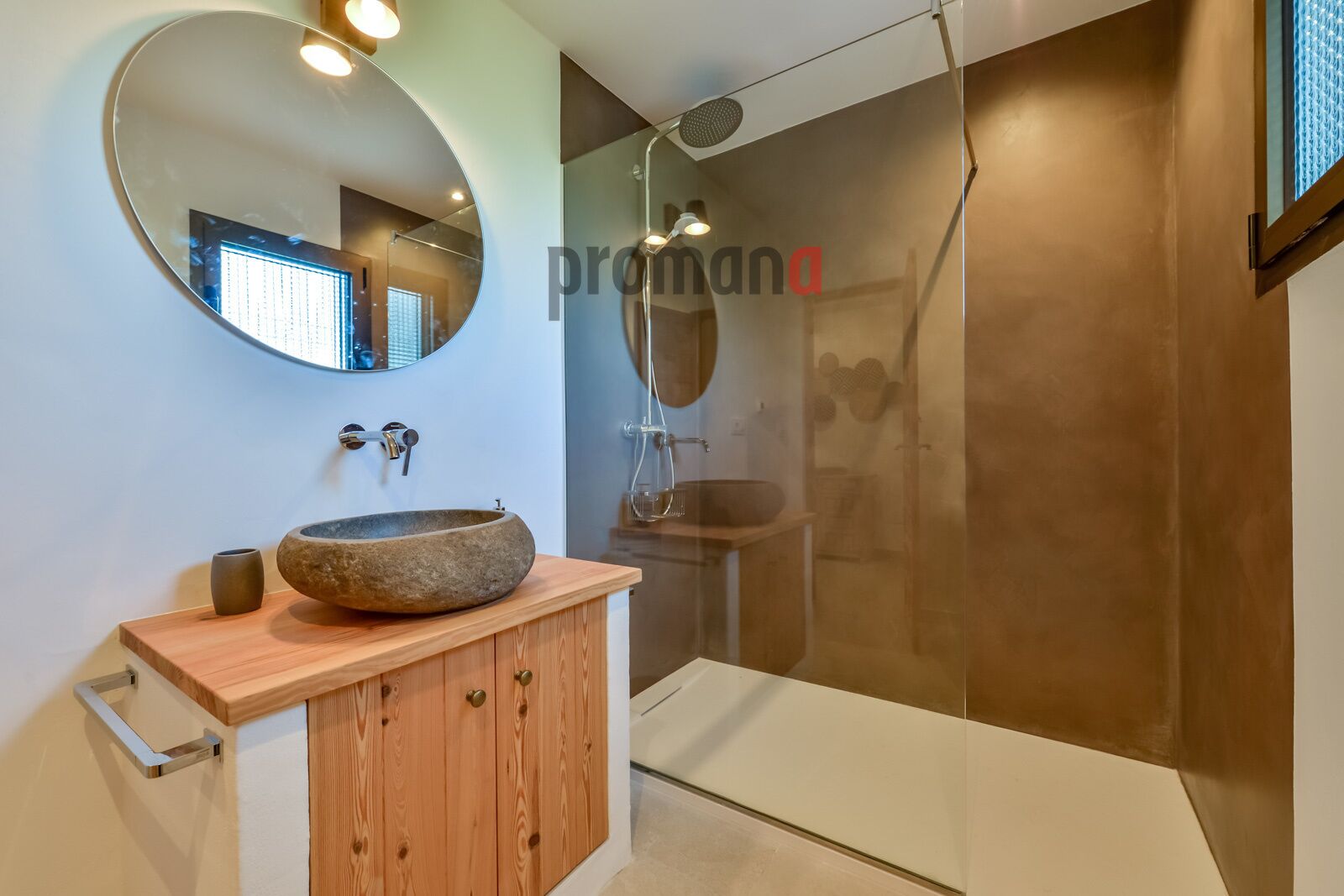 A modern bathroom with a round mirror, wooden vanity, and a stone basin.