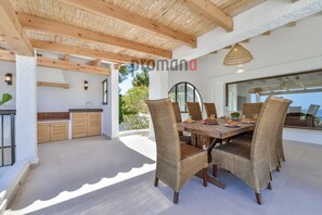 Un vaste espace à manger avec une table en bois et des chaises en osier, une cuisine dotée de meubles en bois et une grande fenêtre offrant une vue sur l’extérieur.