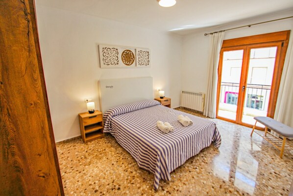 A bedroom with a striped bedspread, wooden nightstands, a radiator, and a view through a glass door.