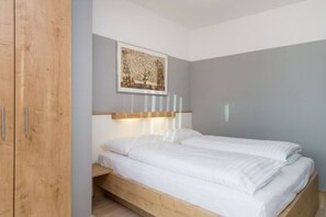 Un dormitorio con estructura de cama de madera, cabecera con lámpara y armario de madera. Se aprecia una obra de arte enmarcada en la pared.