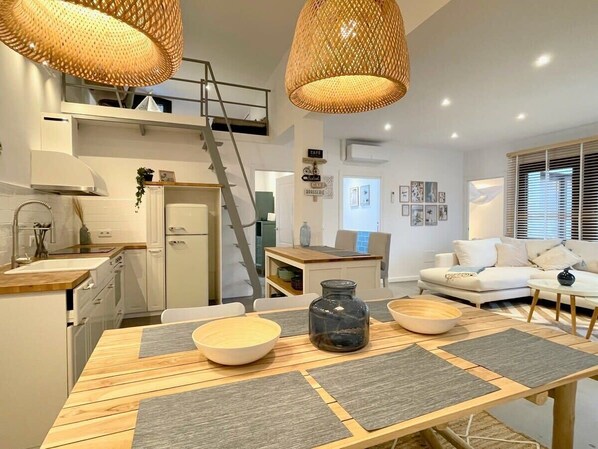 A modern kitchen with a dining area, a staircase, and a living room with a sofa and a coffee table.