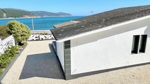 Un bâtiment blanc avec un toit en tuiles, une allée gravillonnée et une vue sur la mer et les collines en arrière-plan.