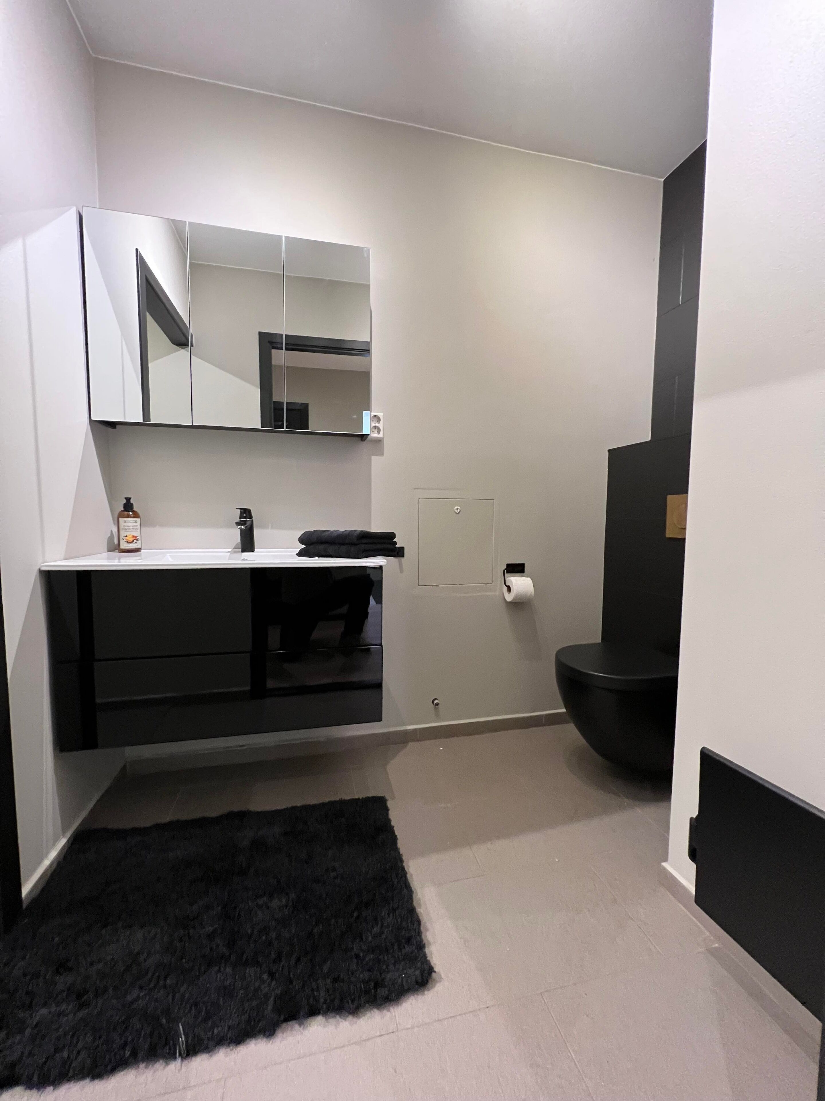 A modern bathroom with a black bathtub, a white sink with a mirror above it, and a black rug on the floor.