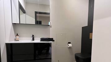 A modern bathroom with a black bathtub, a white sink with a mirror above it, and a black rug on the floor.