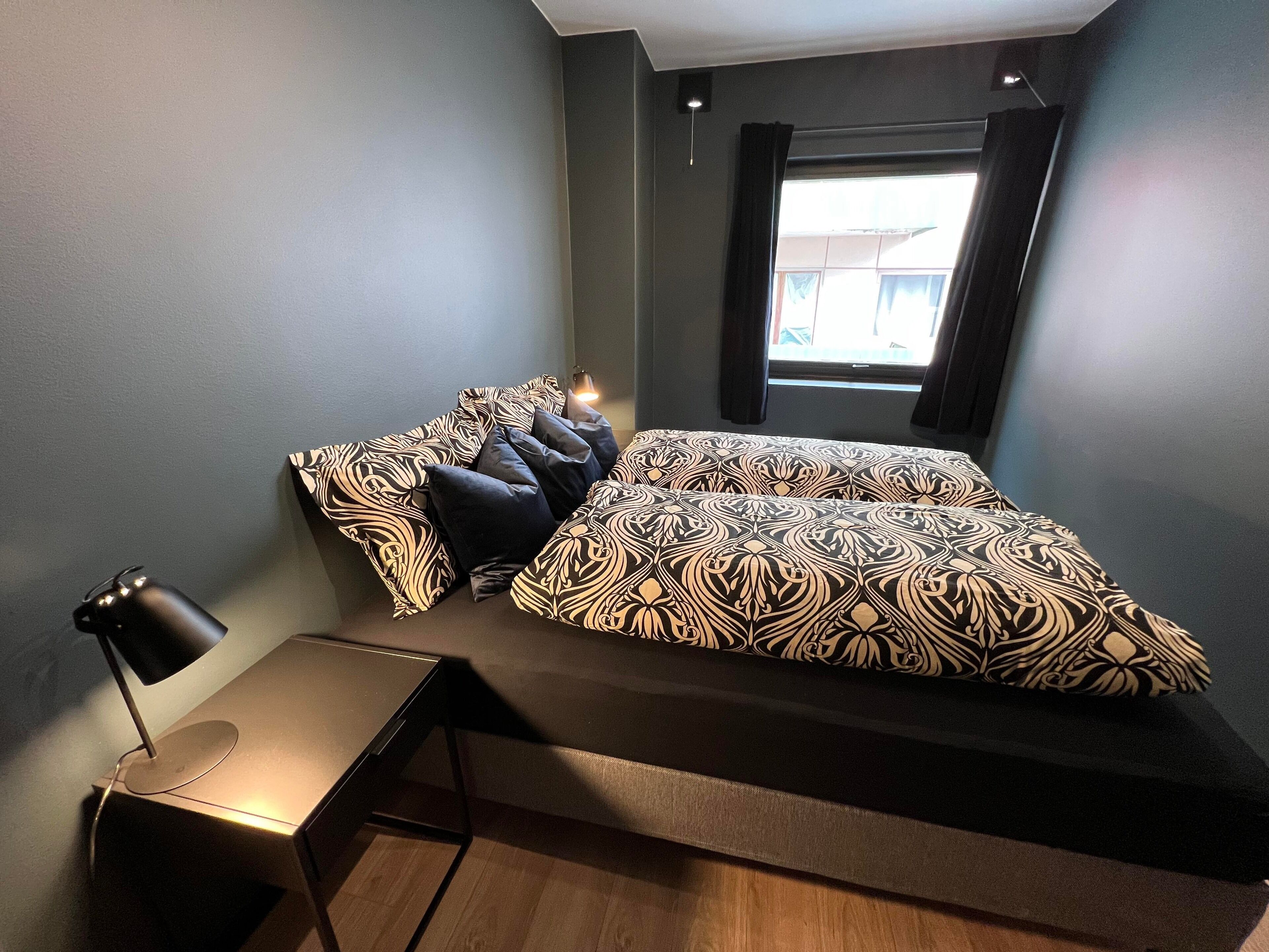 A modern bedroom with a large bed, a desk, and a window.
