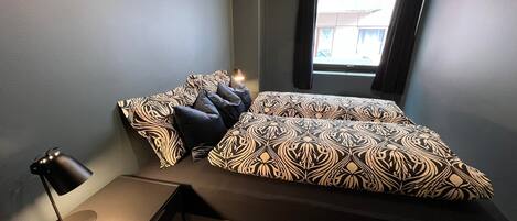 A modern bedroom with a large bed, a desk, and a window.