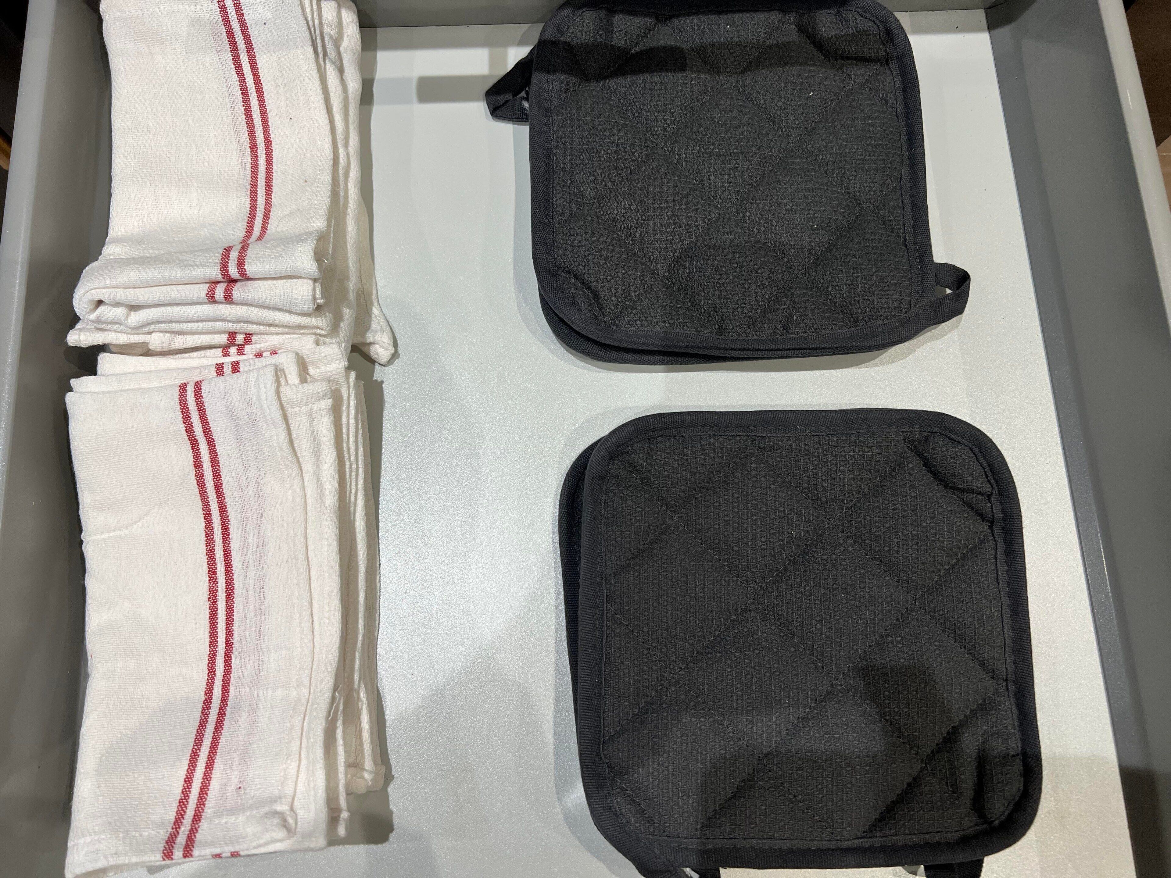 A neatly arranged drawer with folded white towels with red stripes and two black toiletry bags.