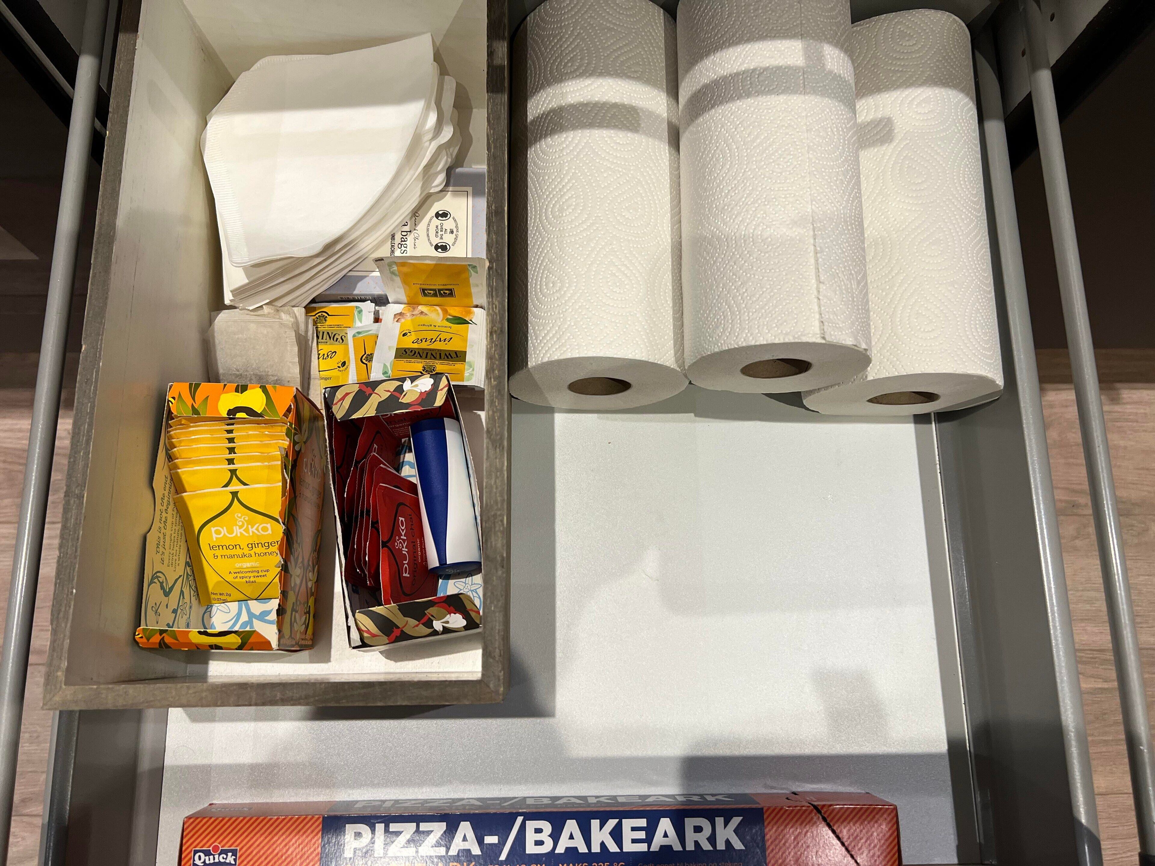 A storage area with various items including paper towels, boxes of lemon ginger tea, and a pizza/bakeark box.