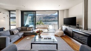 Una sala moderna con sofá, mesa de centro y televisor, un balcón con vistas a montañas y una chimenea.