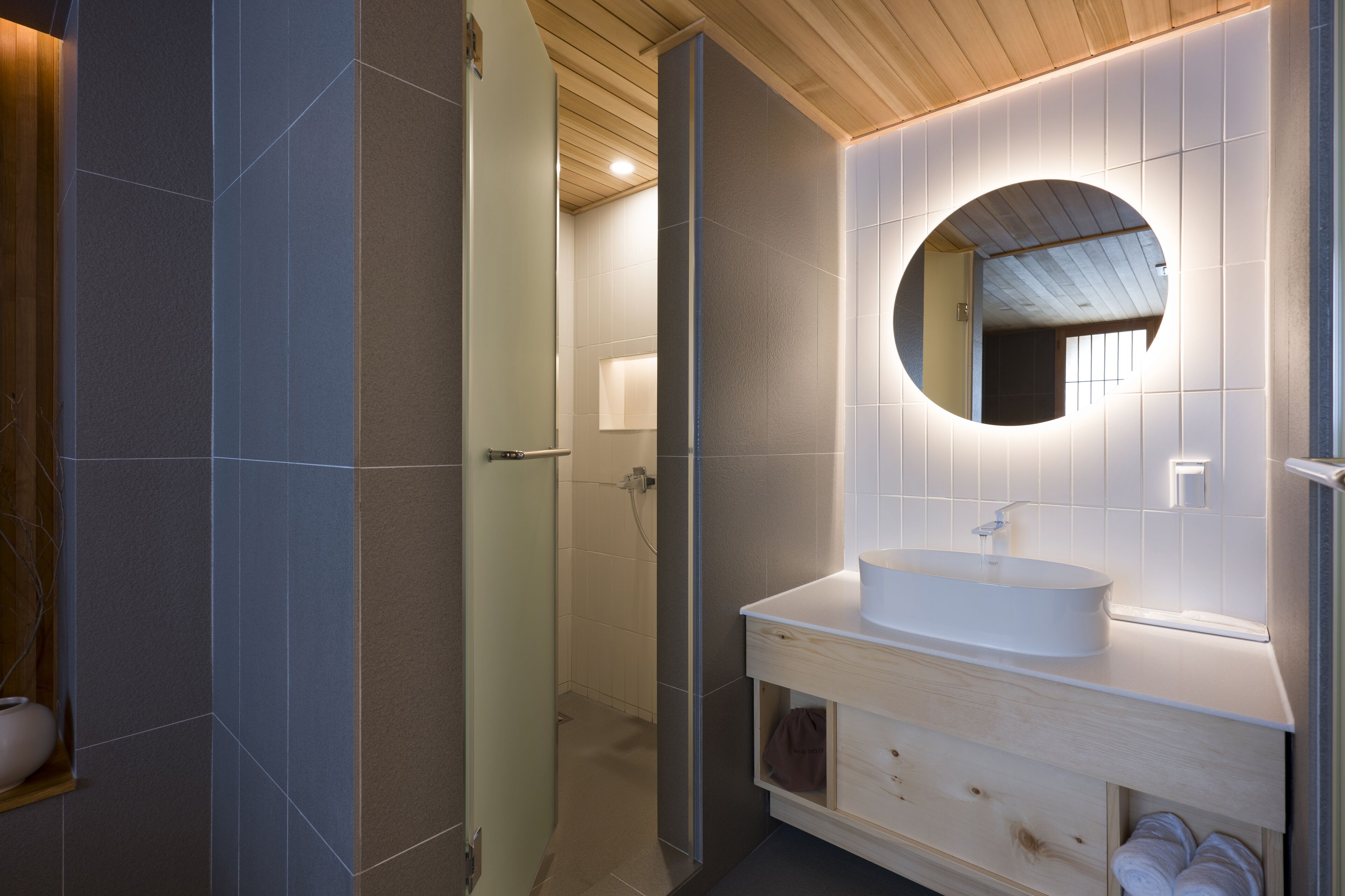 A modern bathroom with a large mirror, a white sink, and a wooden vanity.