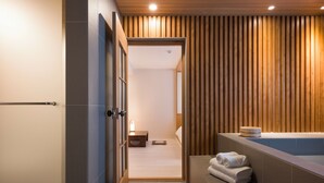 A modern bathroom with a wooden panel wall, a bathtub, and a small bedside table with a lamp. - HOTEL YUSURIM (Changwon)