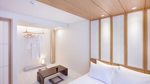 A modern hotel room with a wooden ceiling, a bed with white linens, a bedside table with a cup, and a clothing rack with white robes. - HOTEL YUSURIM (Changwon)