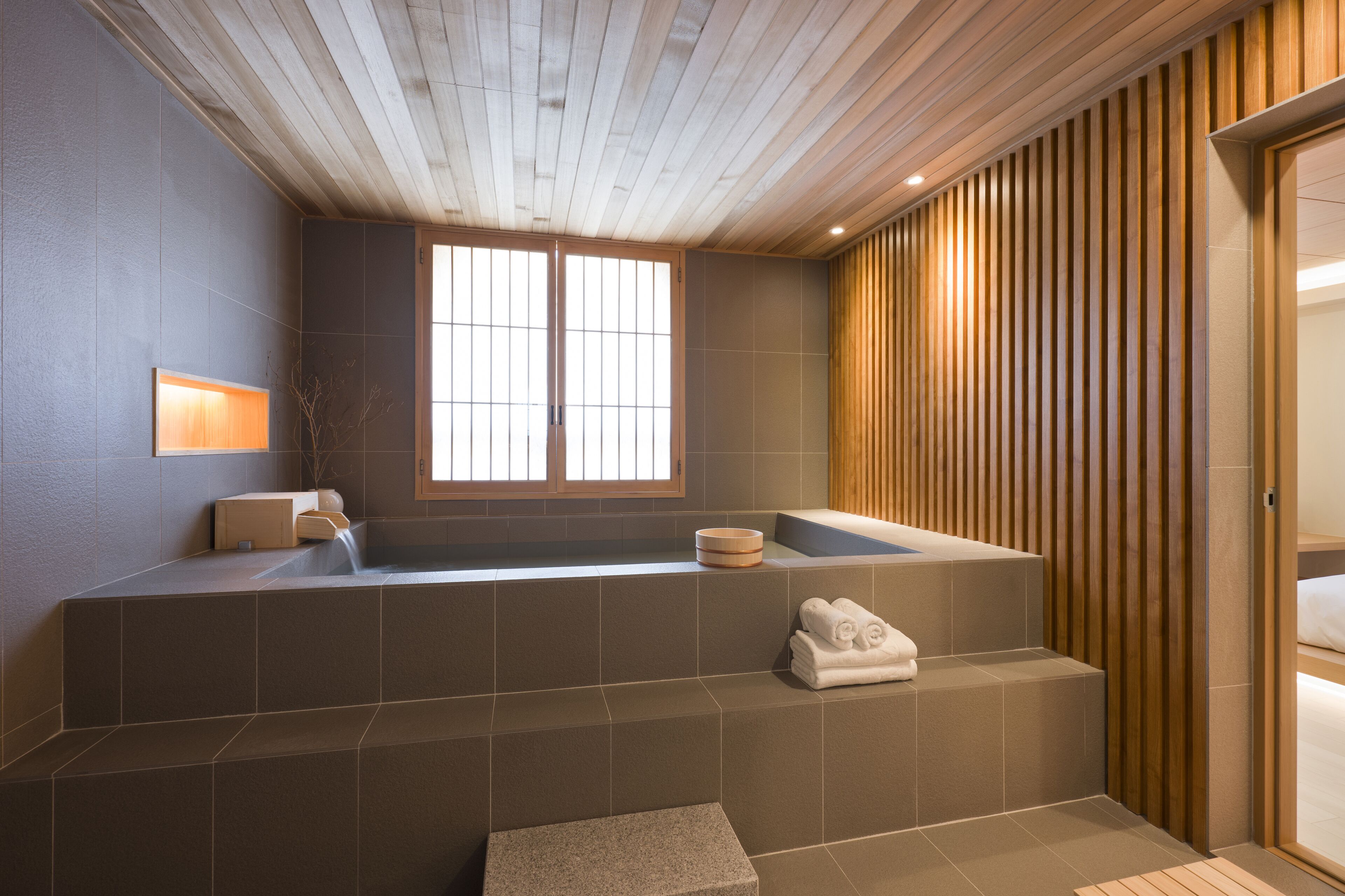 A modern bathroom with a wooden ceiling, a large bathtub, and a window.