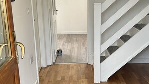 Um corredor com piso de madeira, um tapete de entrada cinza e uma escada branca com carpete cinza.