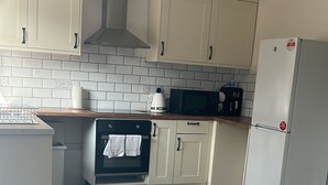 Cozinha moderna com armários brancos, forno embutido, micro-ondas e geladeira.