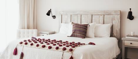 Un lit bien fait, avec une couette blanche, un oreiller à rayures et un plaid décoratif orné de glands.