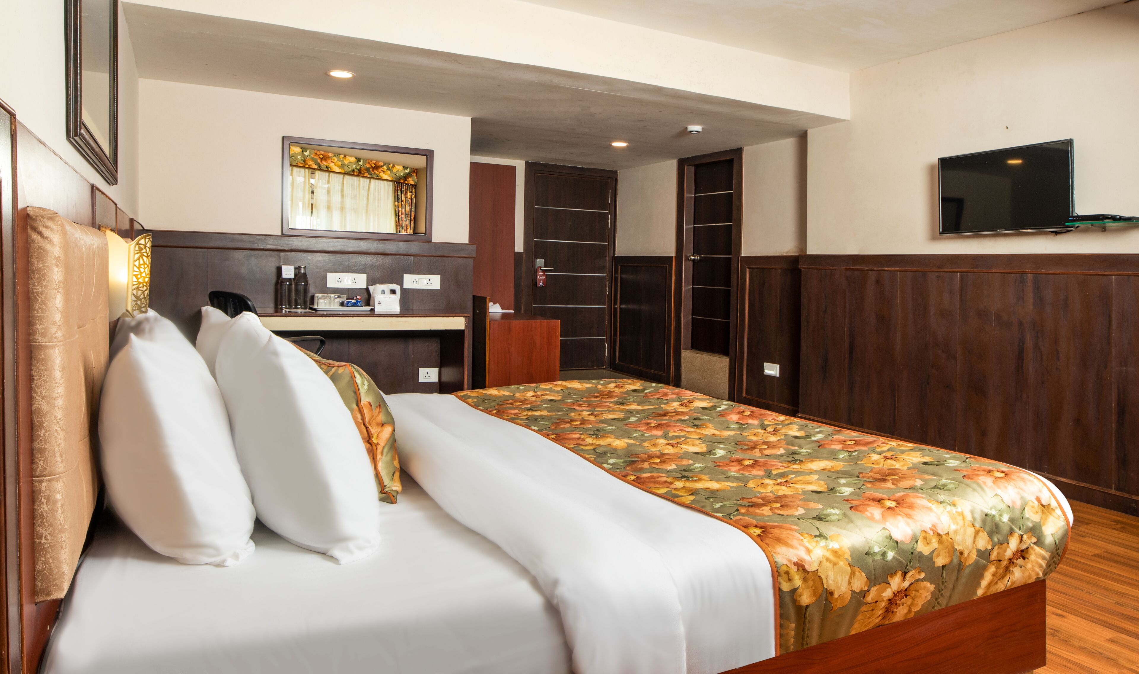 A hotel room with a bed, a desk, a mirror, a wardrobe, and a TV.