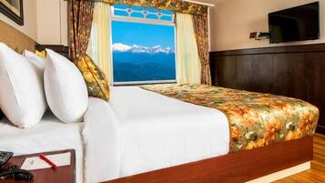 A hotel room with a large bed, a view of mountains, a flat-screen TV, and a desk with a telephone.