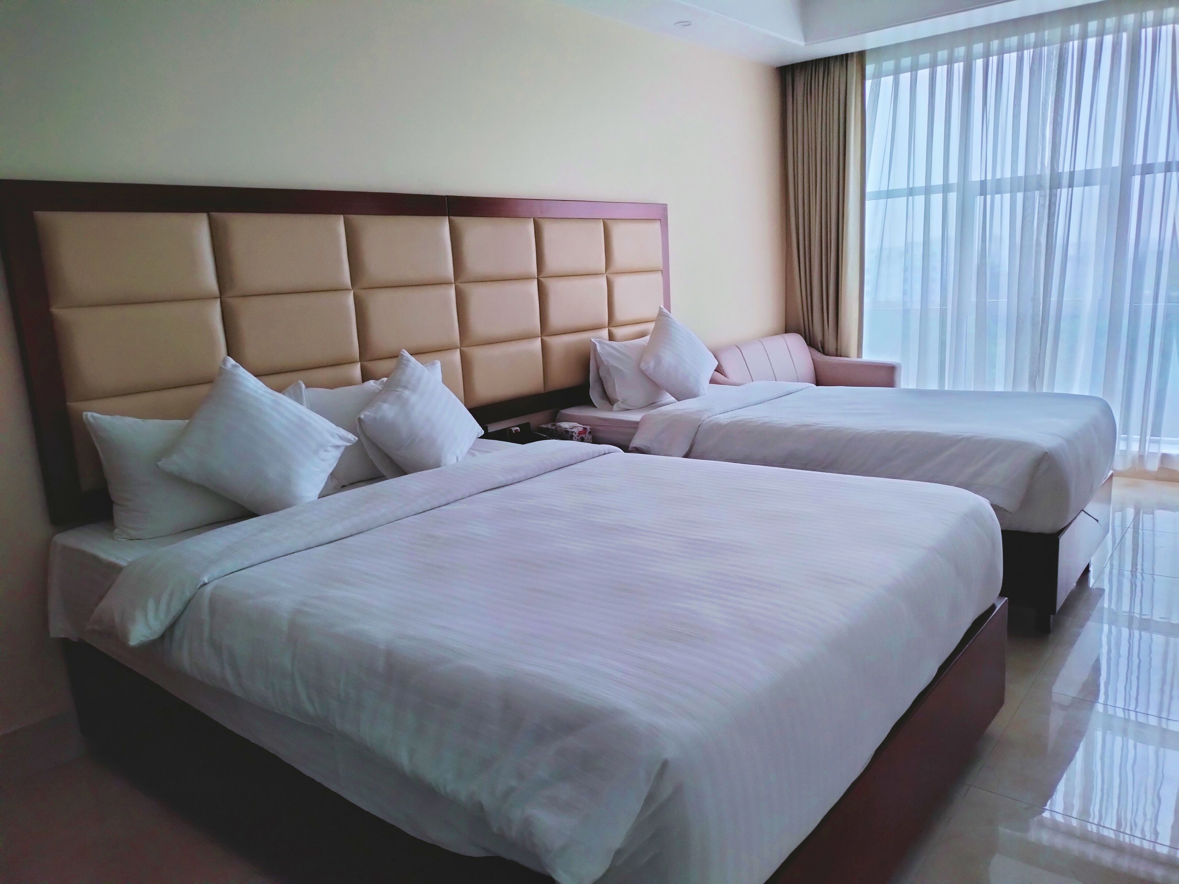A hotel room with two beds, each with a headboard, white bedding, and a nightstand.