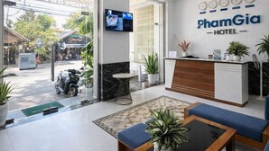 A hotel lobby with a reception desk, seating area, ceiling fan, and a TV screen. - Pham Gia Hotel Mui Ne (Mui Ne)