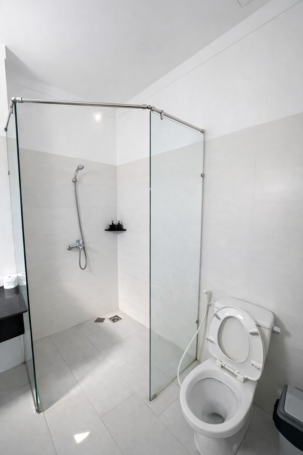 Un baño moderno con cabina de ducha de vidrio, inodoro y un estante pequeño con artículos de aseo.