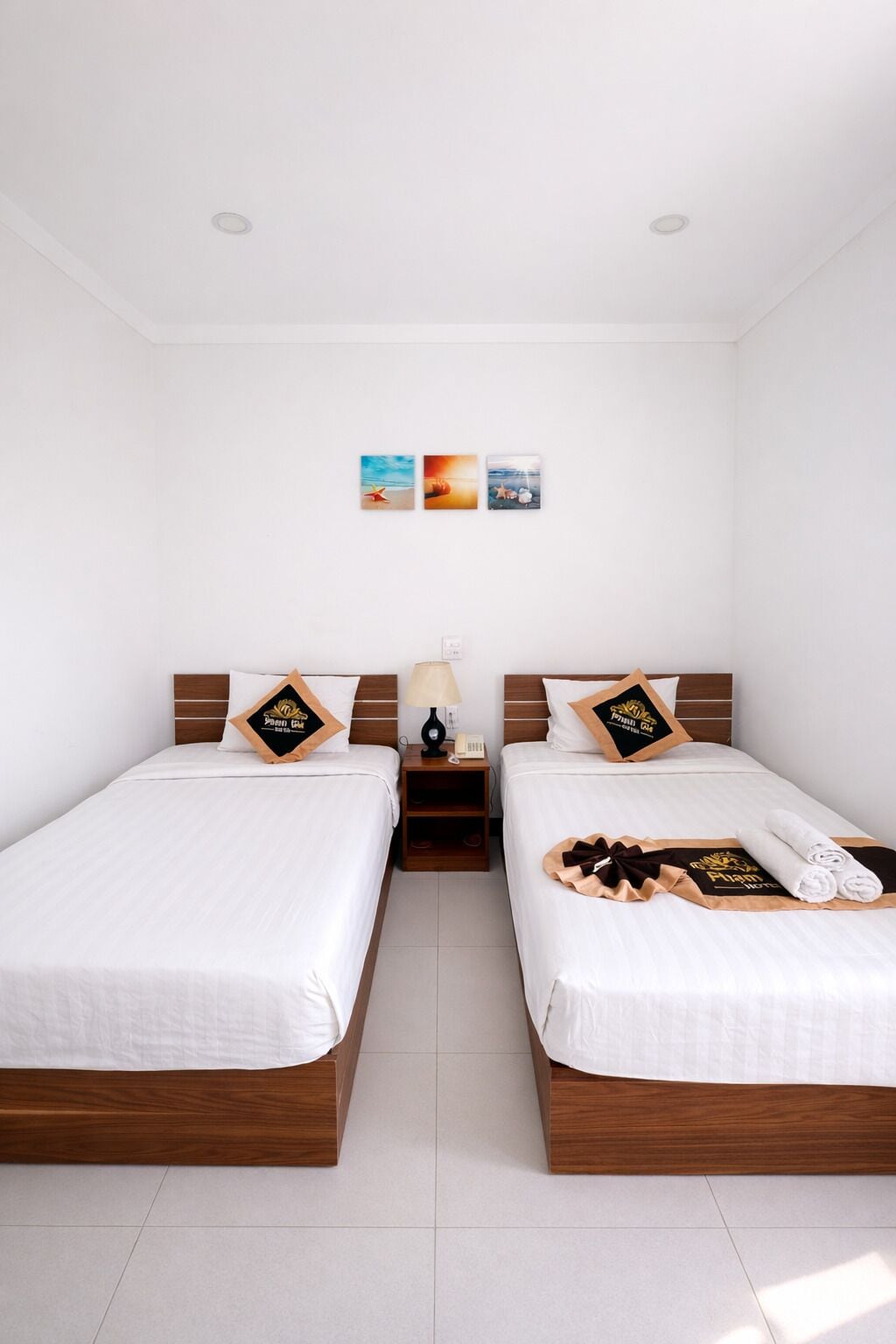 A hotel room with two beds, a nightstand, a lamp, and three wall art pieces.