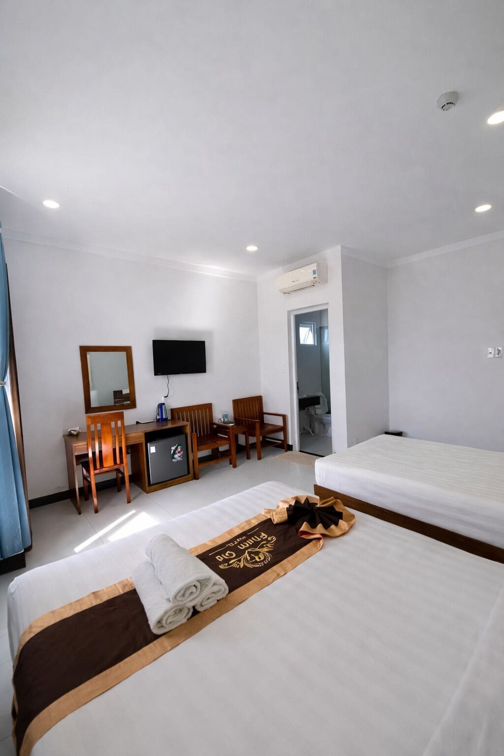 A hotel room with a bed, a desk with a chair, a television, and an air conditioning unit.