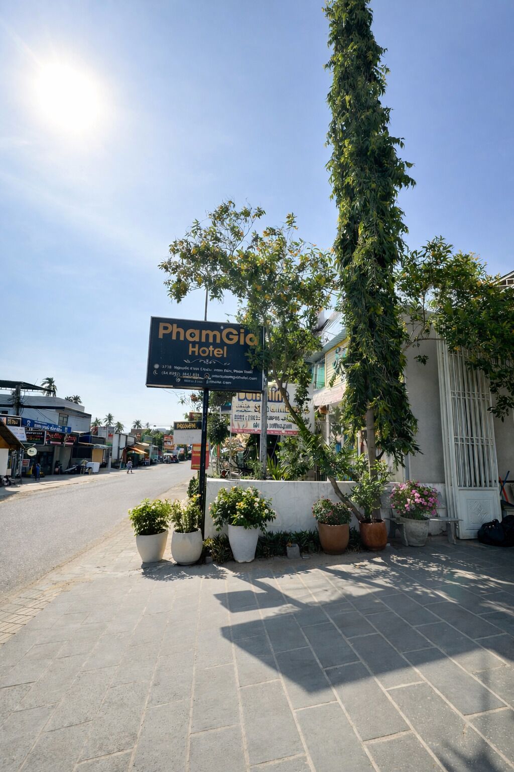 Une enseigne d’hôtel, des tables et chaises à l’extérieur et des plantes en pot.