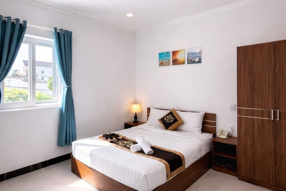 Quarto de hotel com uma cama, um guarda-roupa, uma mesa de cabeceira e uma janela com cortinas.