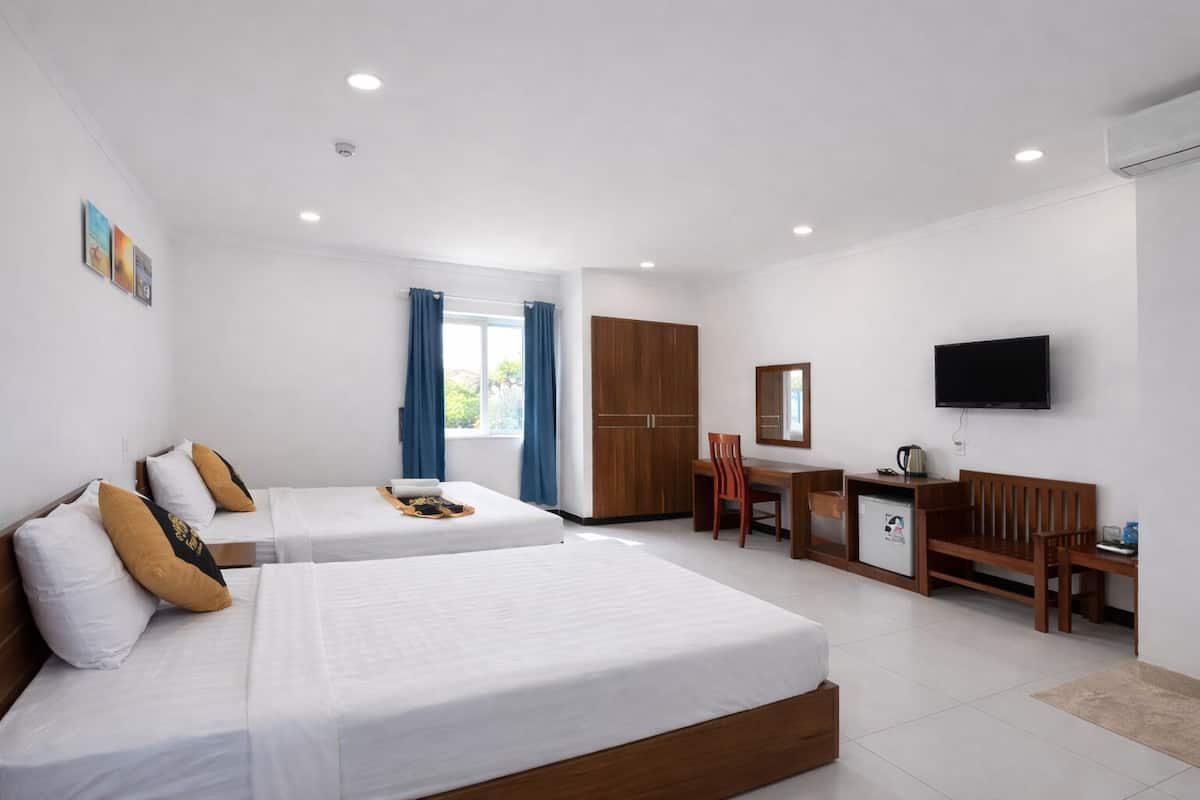 Quarto de hotel com duas camas, uma escrivaninha, uma cadeira, uma TV e um guarda-roupa.