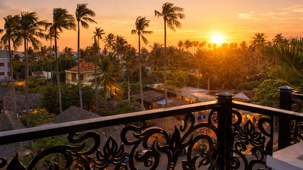 A sunset view from a balcony with palm trees and buildings in the background. - Pham Gia Hotel Mui Ne (Mui Ne)