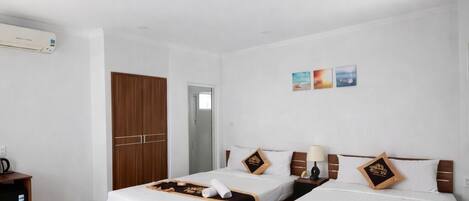 Habitación de hotel con dos camas, un armario, un escritorio y aire acondicionado instalado en la pared.