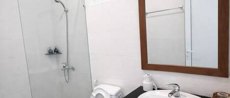 A modern bathroom with a glass shower enclosure, a toilet, a sink with a mirror, and a small window above the toilet.