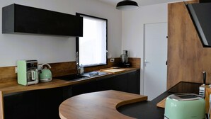 Une cuisine moderne avec un plan de travail noir, une bouilloire verte, un grille-pain et une machine à café.