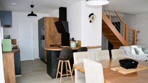 Une cuisine moderne dotée d’un îlot central, d’un coin repas avec une table et des chaises en bois, et d’un escalier menant à un niveau supérieur.