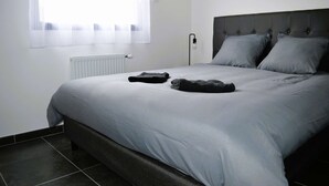 Une chambre à coucher avec un lit, un radiateur, une fenêtre avec des rideaux légers et une lampe de chevet.