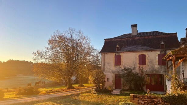 Ein rustikales Haus mit einer Steinaußenwand, roten Fensterläden und einem Schornstein.