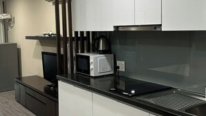 A modern kitchen with white cabinets, a black countertop, a microwave, a kettle, and a built-in oven.