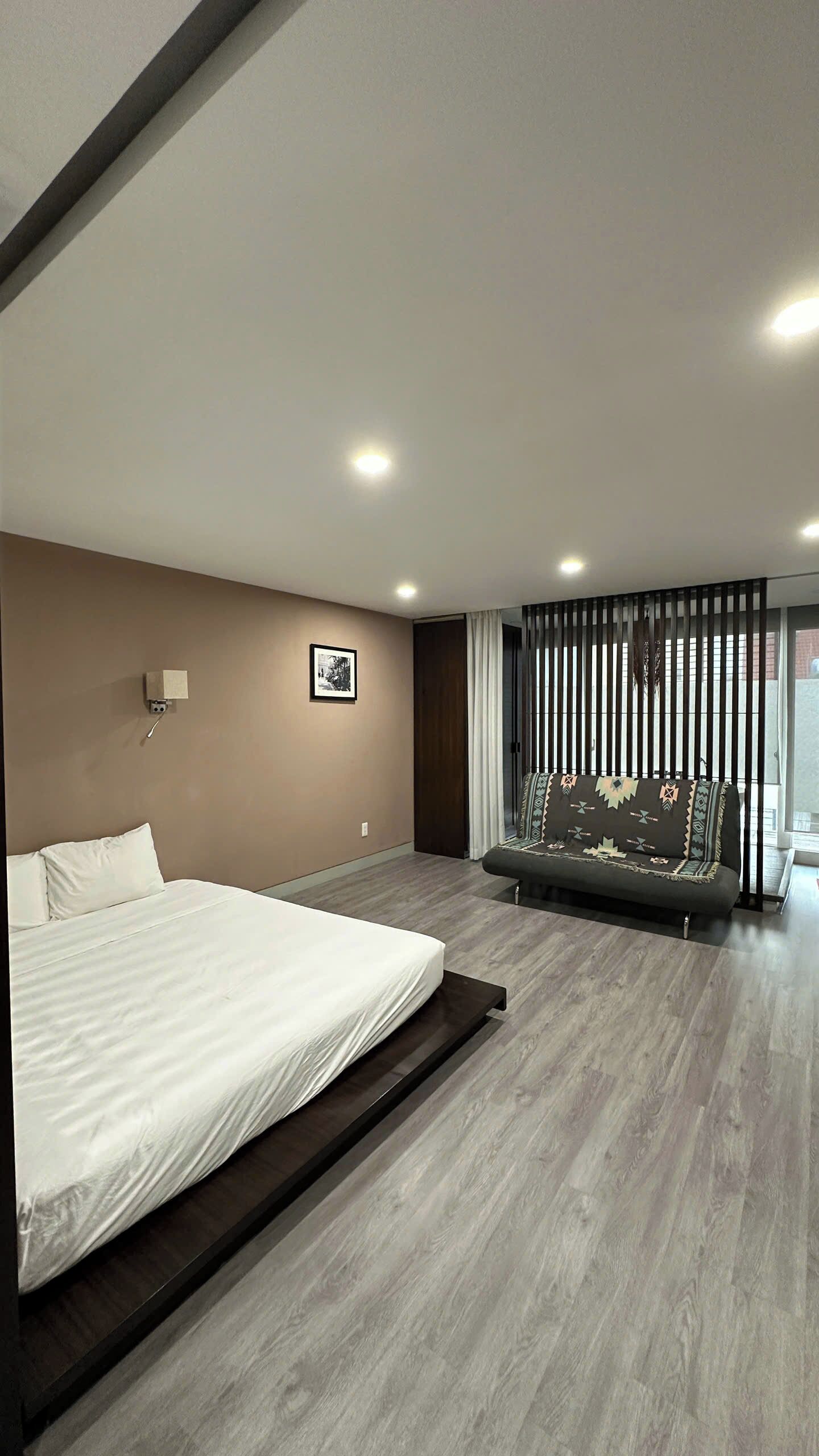 A modern bedroom with a large bed, a wall-mounted light, and a window with blinds.