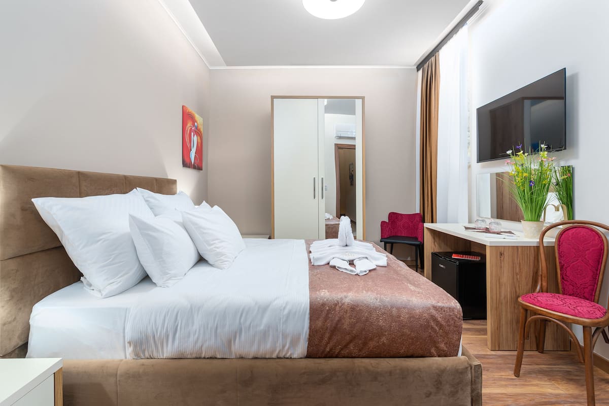 A modern hotel room with a large bed, a desk with a chair, a TV, and a mirror.