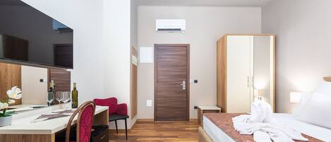 Una habitación de hotel moderna con piso de madera, un escritorio con silla, una cama con cabecera, un armario y un espejo grande.