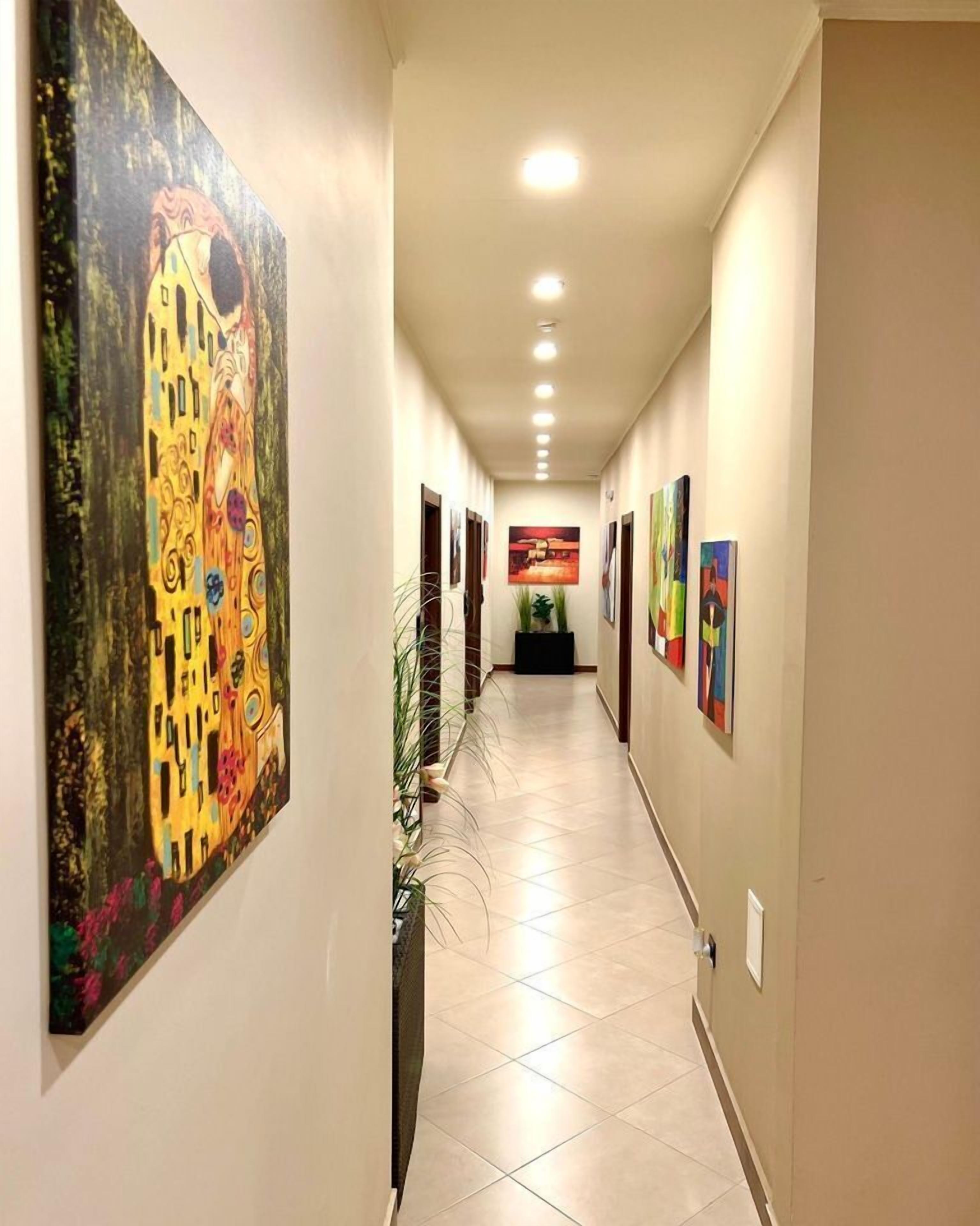 A hallway with artwork on the walls, a tiled floor, and recessed lighting.
